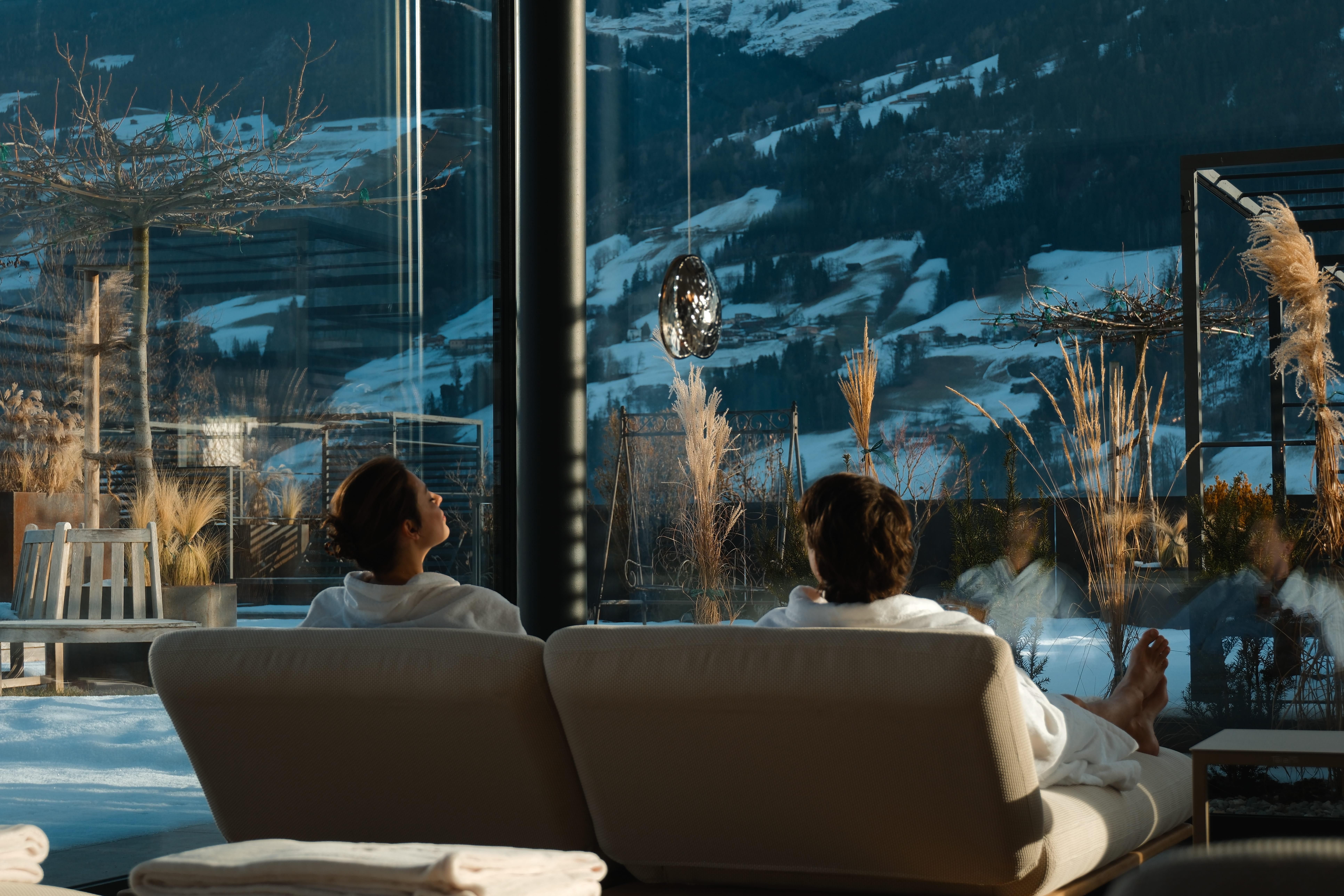 A relaxing spa area with two people in bathrobes. In the background, a beautiful mountain landscape can be seen.