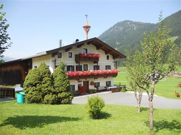 A traditional house with flower boxes and a beautiful garden. Gentle mountains can be seen in the background.