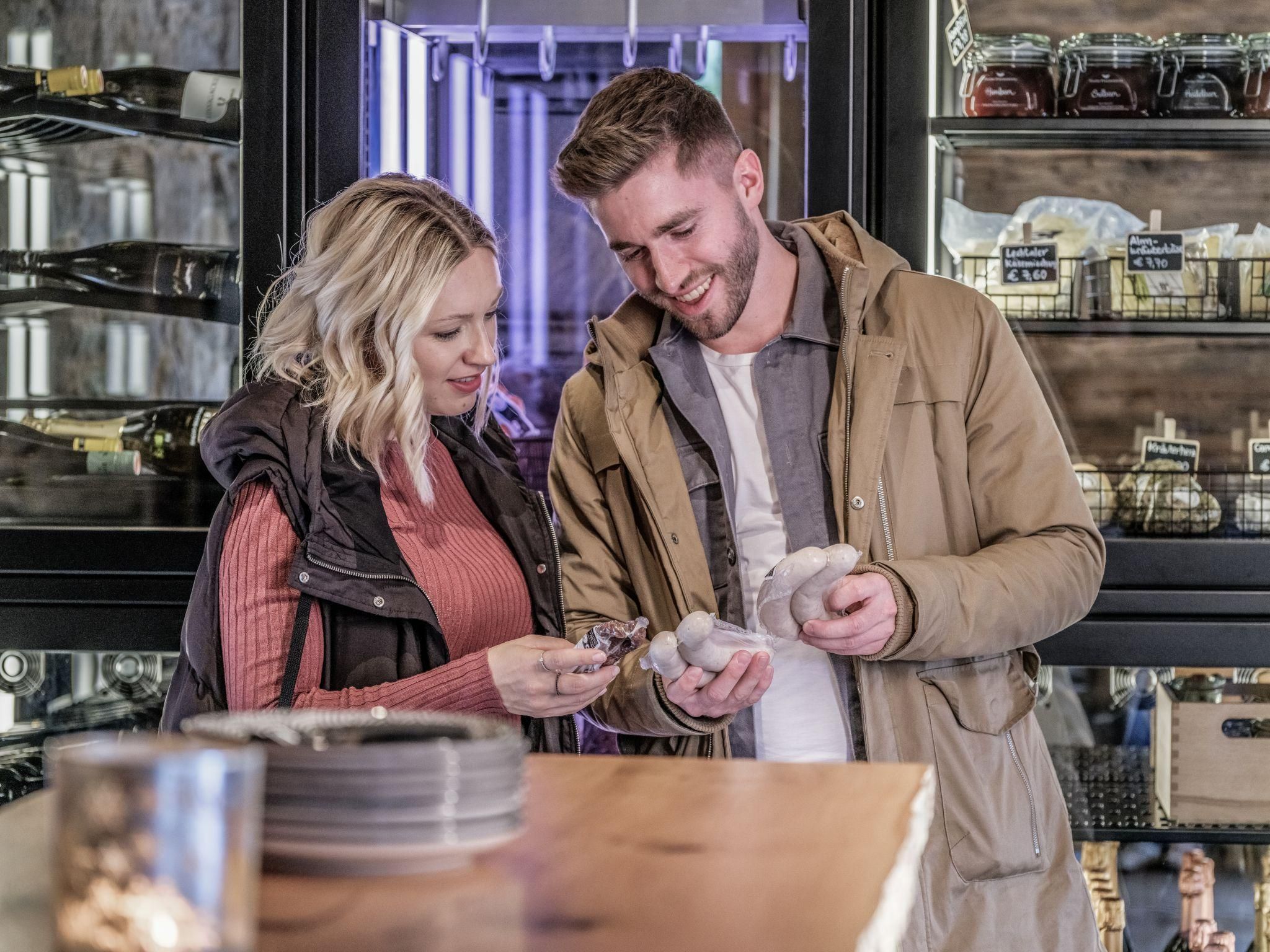 A couple is smiling as they look at products while standing in the enjoyment factory. In the background, shelves with various items are visible.