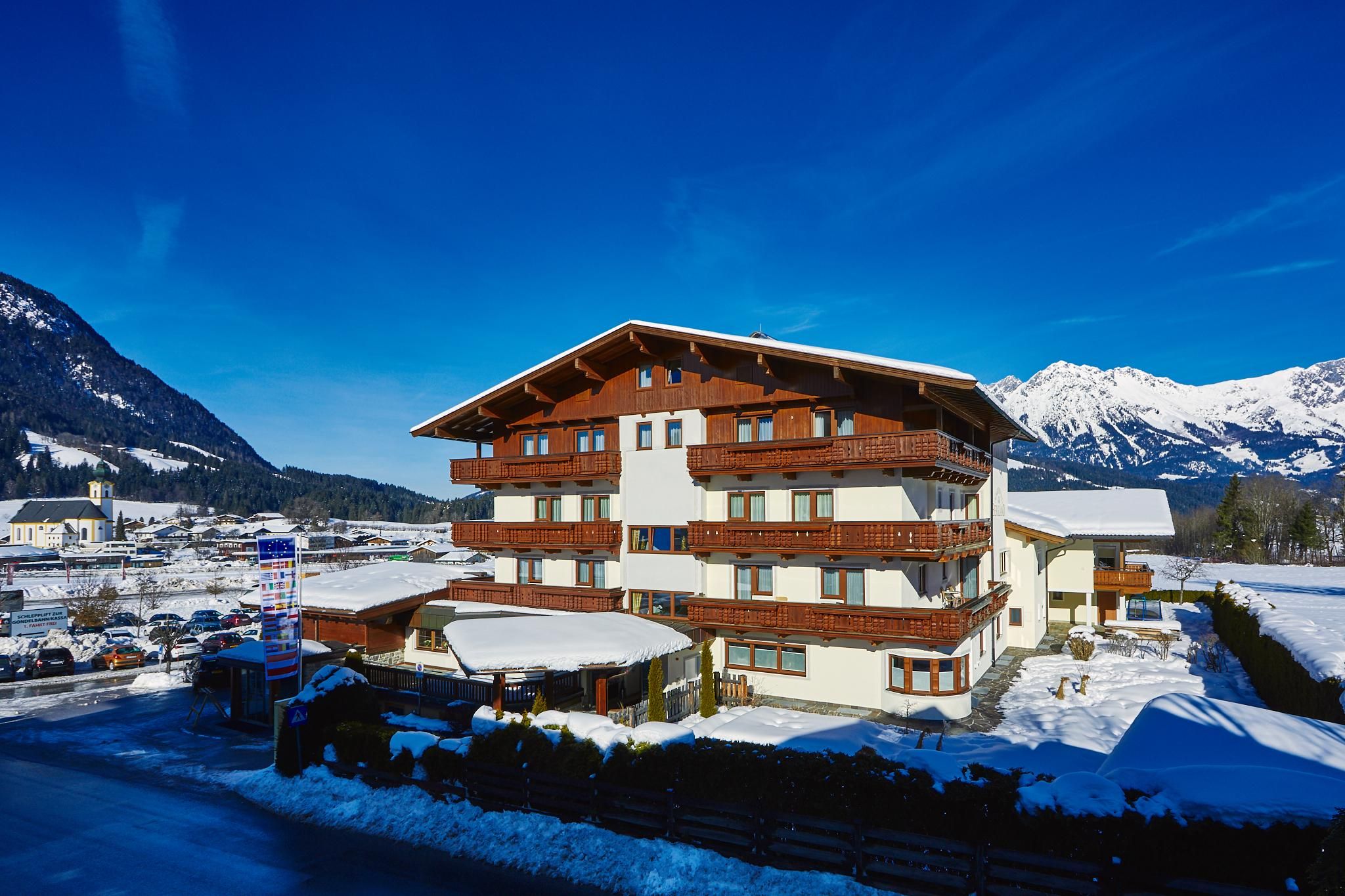 A charming building in Alpine style surrounded by snow and mountains. The sky is clear and blue, creating an inviting atmosphere.