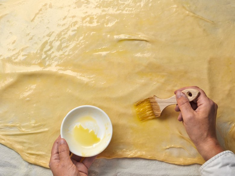 Step 5: Place the dough on a teatowel covered with a thin layer of flour. Brush melted butter onto the lower section of the dough.