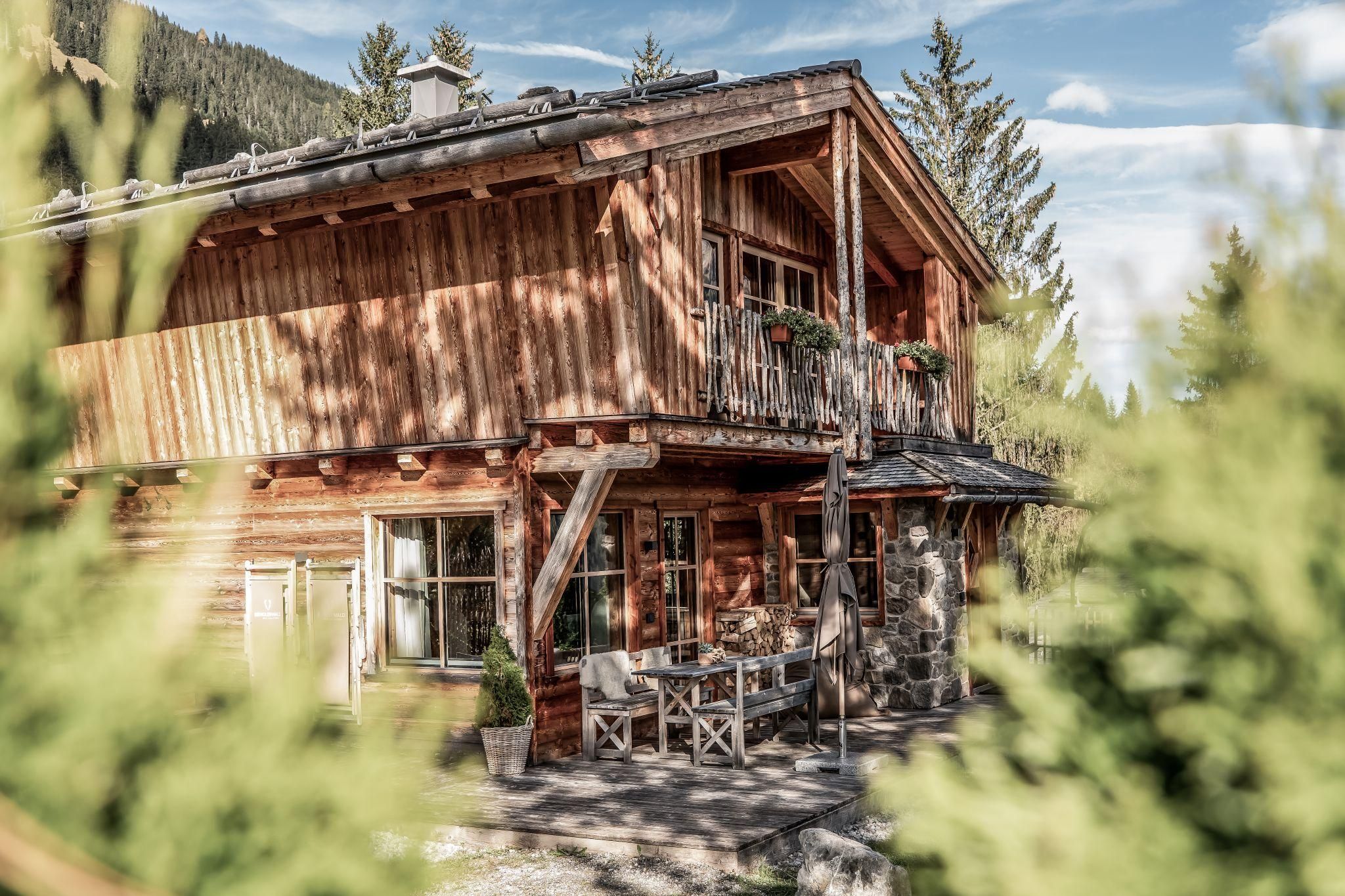 A beautiful chalet surrounded by trees and a picturesque landscape. On the terrace, there are tables and chairs, perfect for relaxed days outdoors.