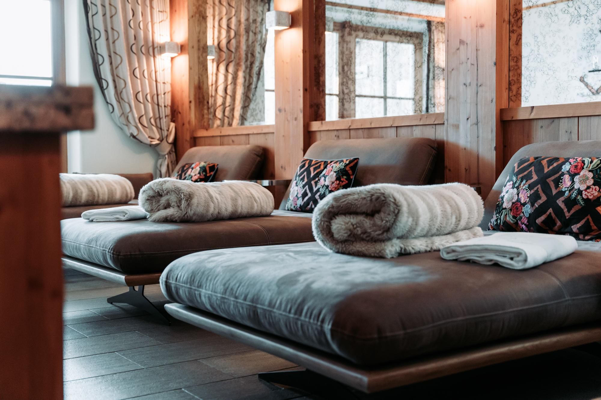 A relaxing wellness area with comfortable loungers and decorative cushions. Soft light and warm wood materials create a cozy atmosphere.