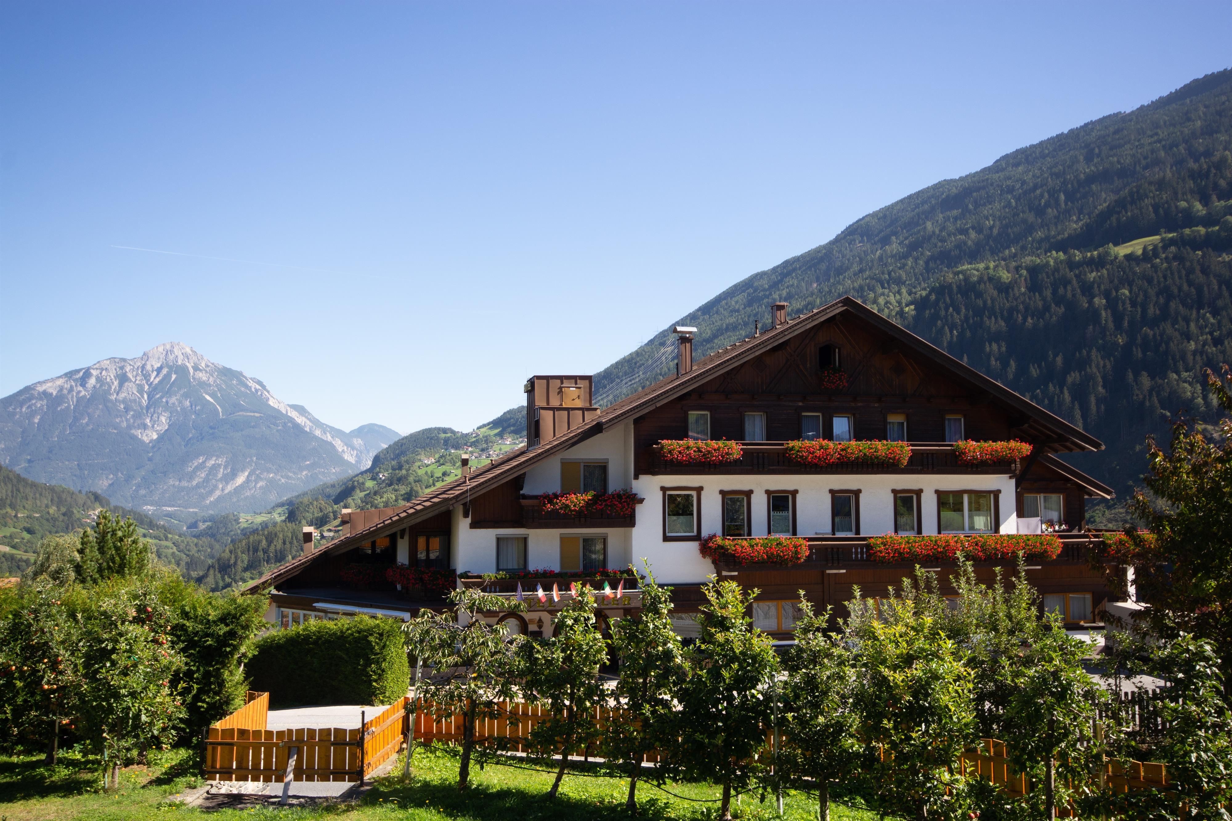 A cozy house in the mountains with blooming balconies. In the background are green hills and snow-capped peaks.