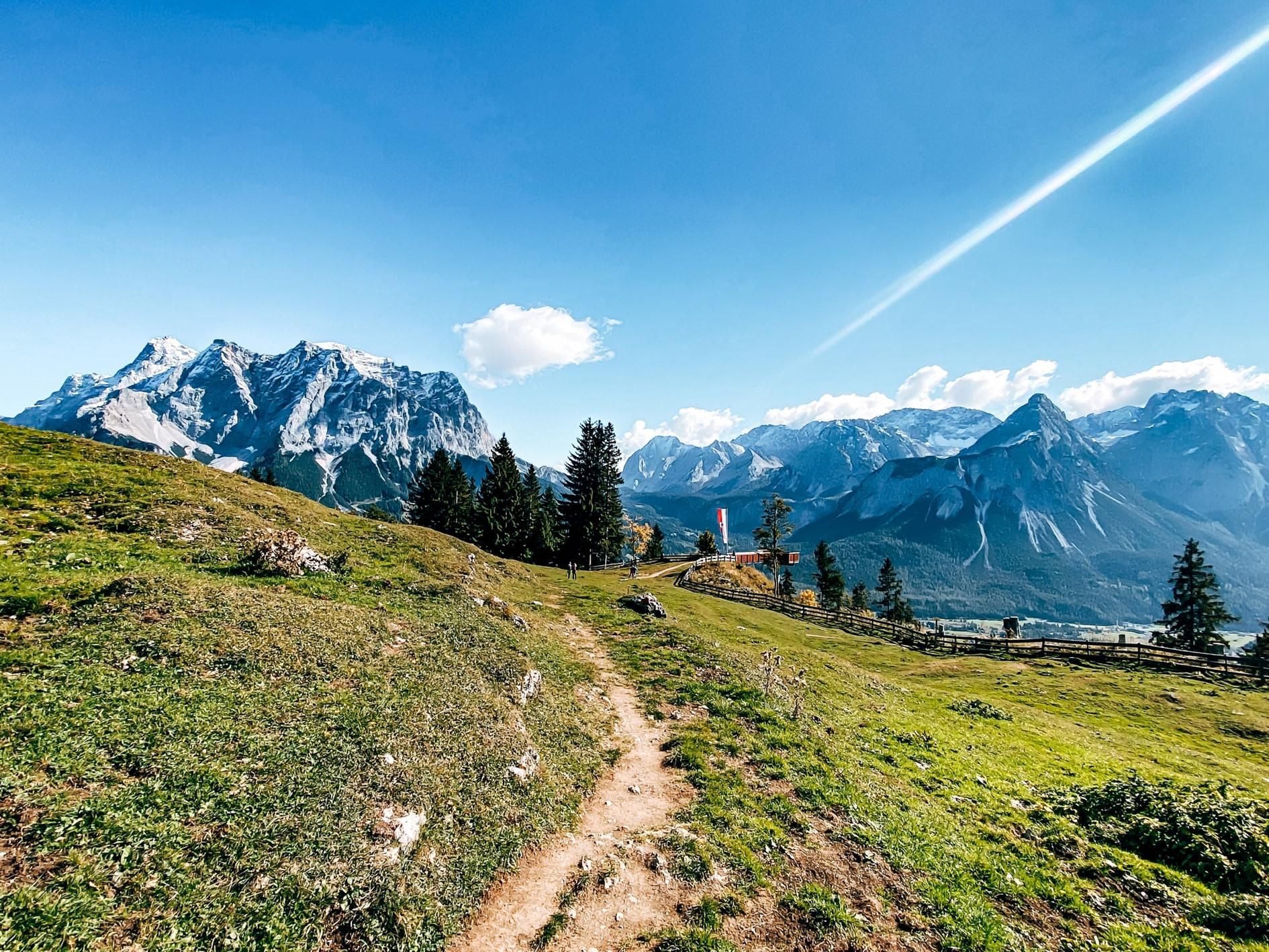 A picturesque mountain landscape with green meadows and high mountains in the background. The sky is clear and blue.