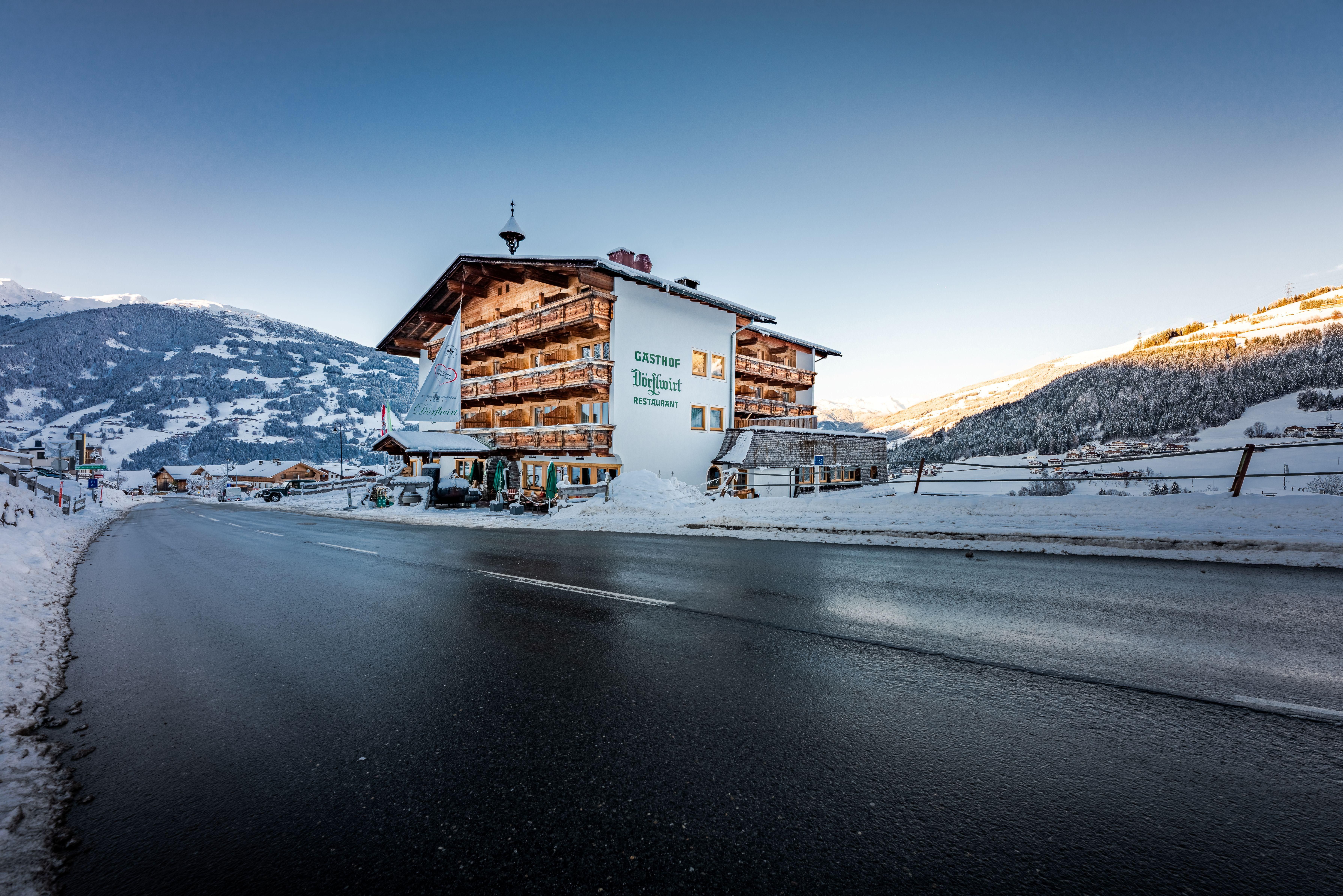 A picturesque hotel in the Alps, surrounded by snow-covered mountains. The road in front of the hotel is freshly cleared and shines in the morning light.