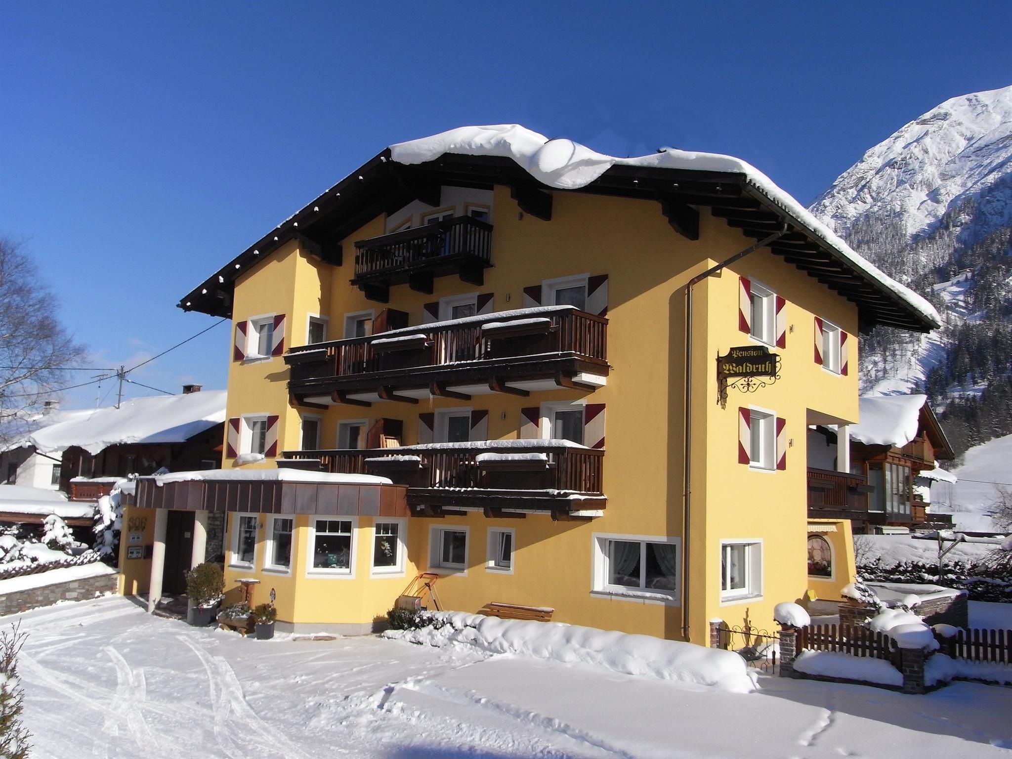 A yellow building in the snow with several balconies. Snow-covered mountains are visible in the background.