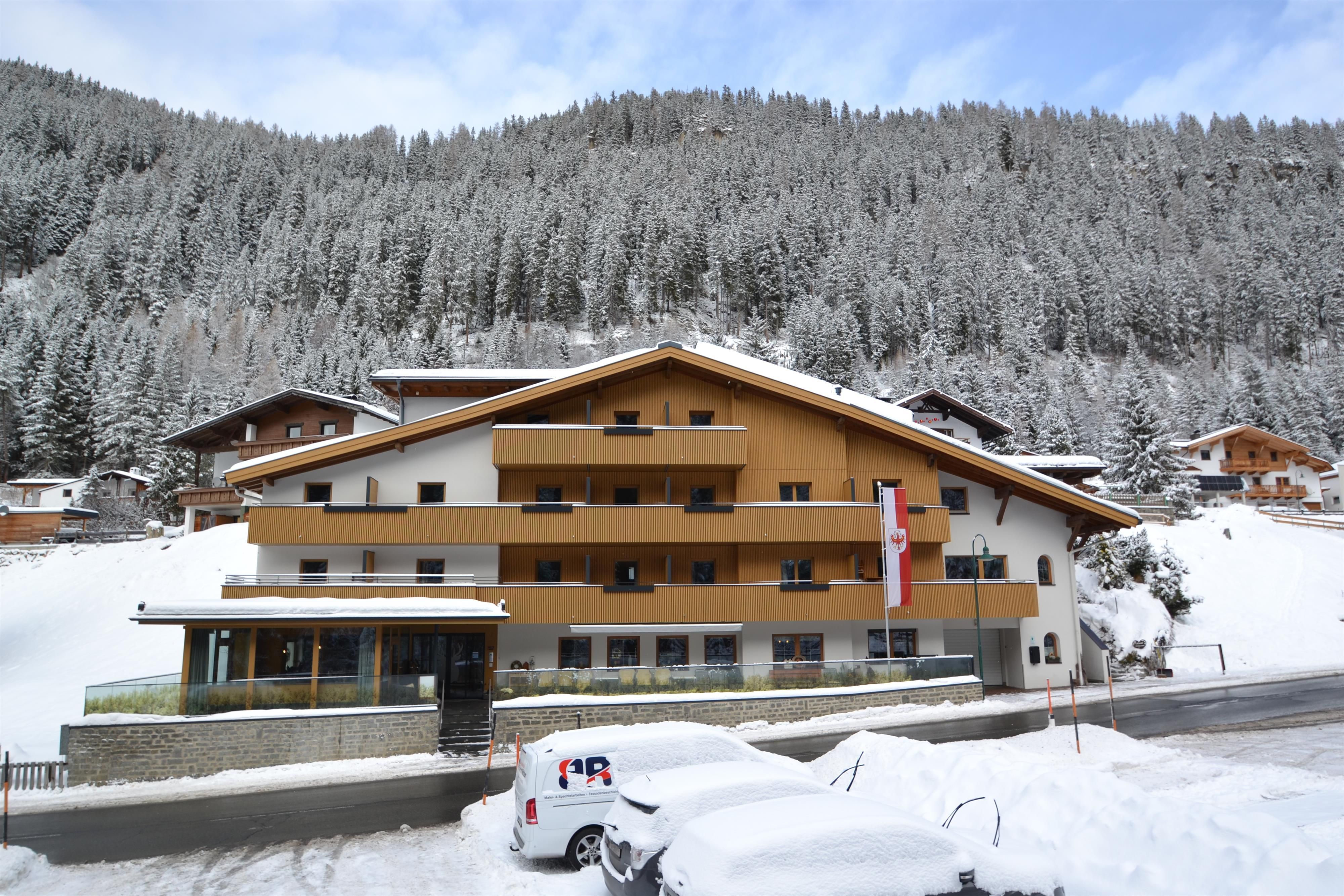A modern building in the snow-covered mountains under a clear blue sky. The surroundings are characterized by tall, snow-covered trees.