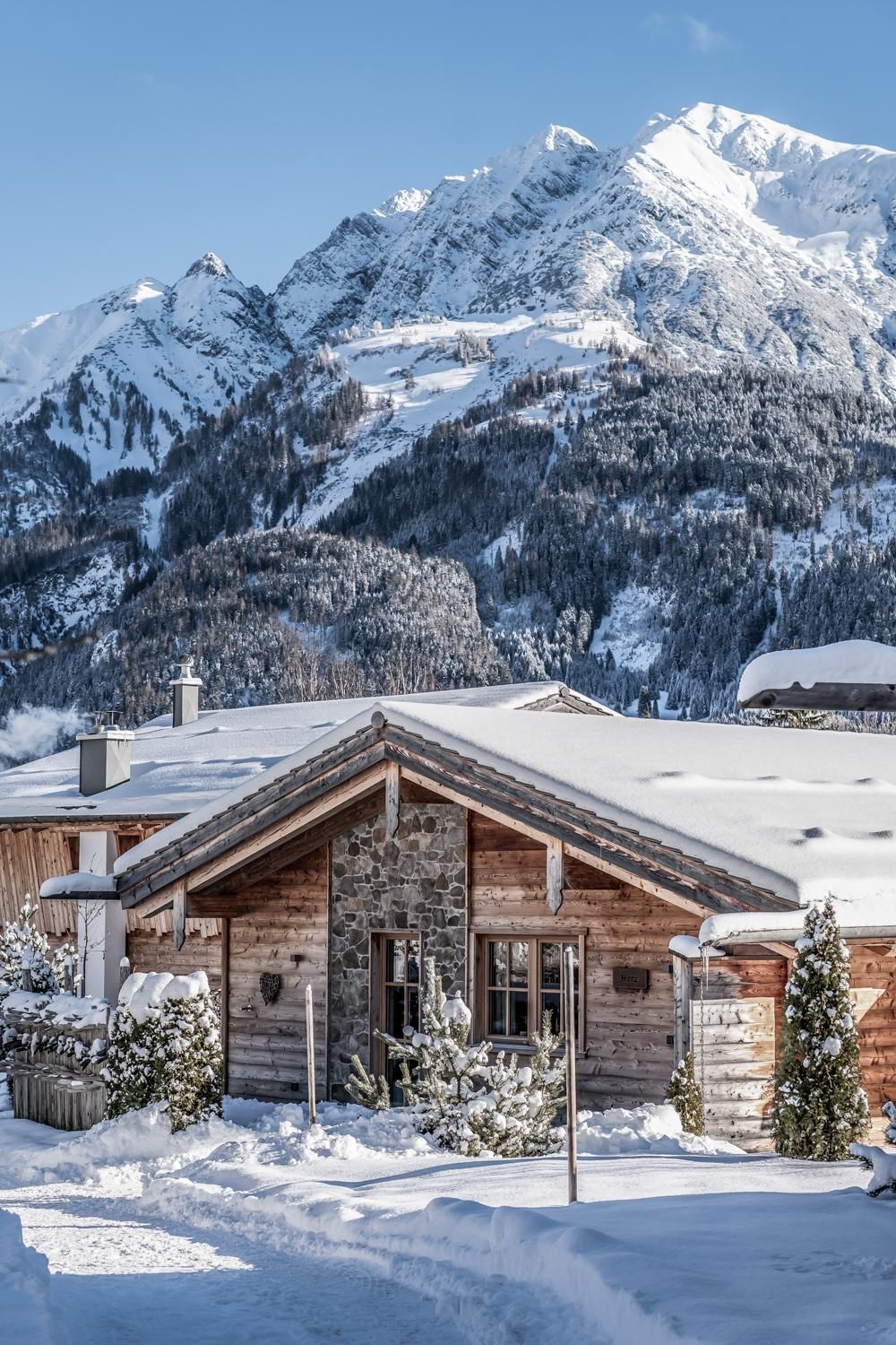 A cozy chalet in the snow, surrounded by snow-covered mountains. The sky is clear and blue, enhancing the wintry atmosphere.
