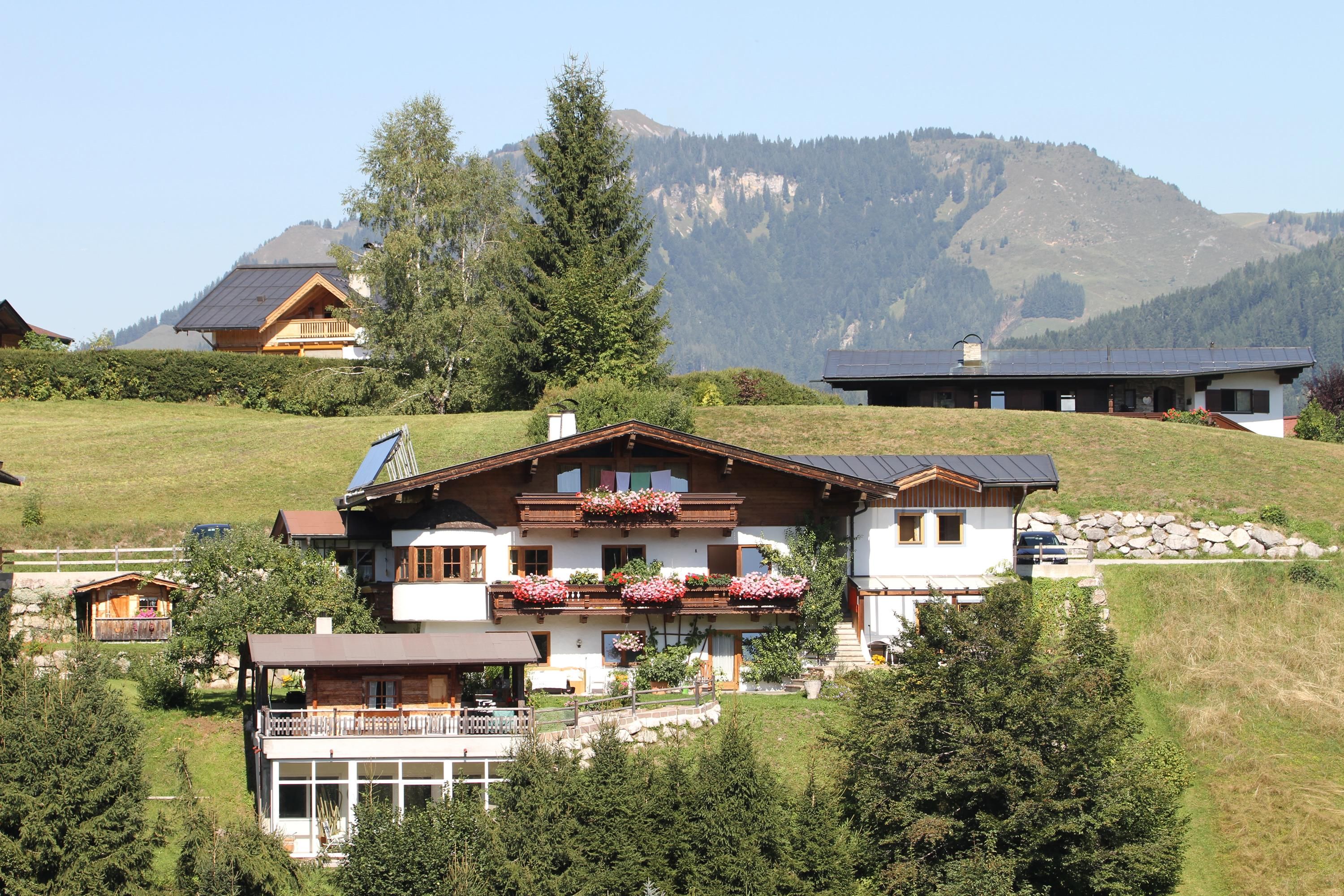 A beautiful house in a green hilly landscape. In the background, there are mountains and a clear sky.