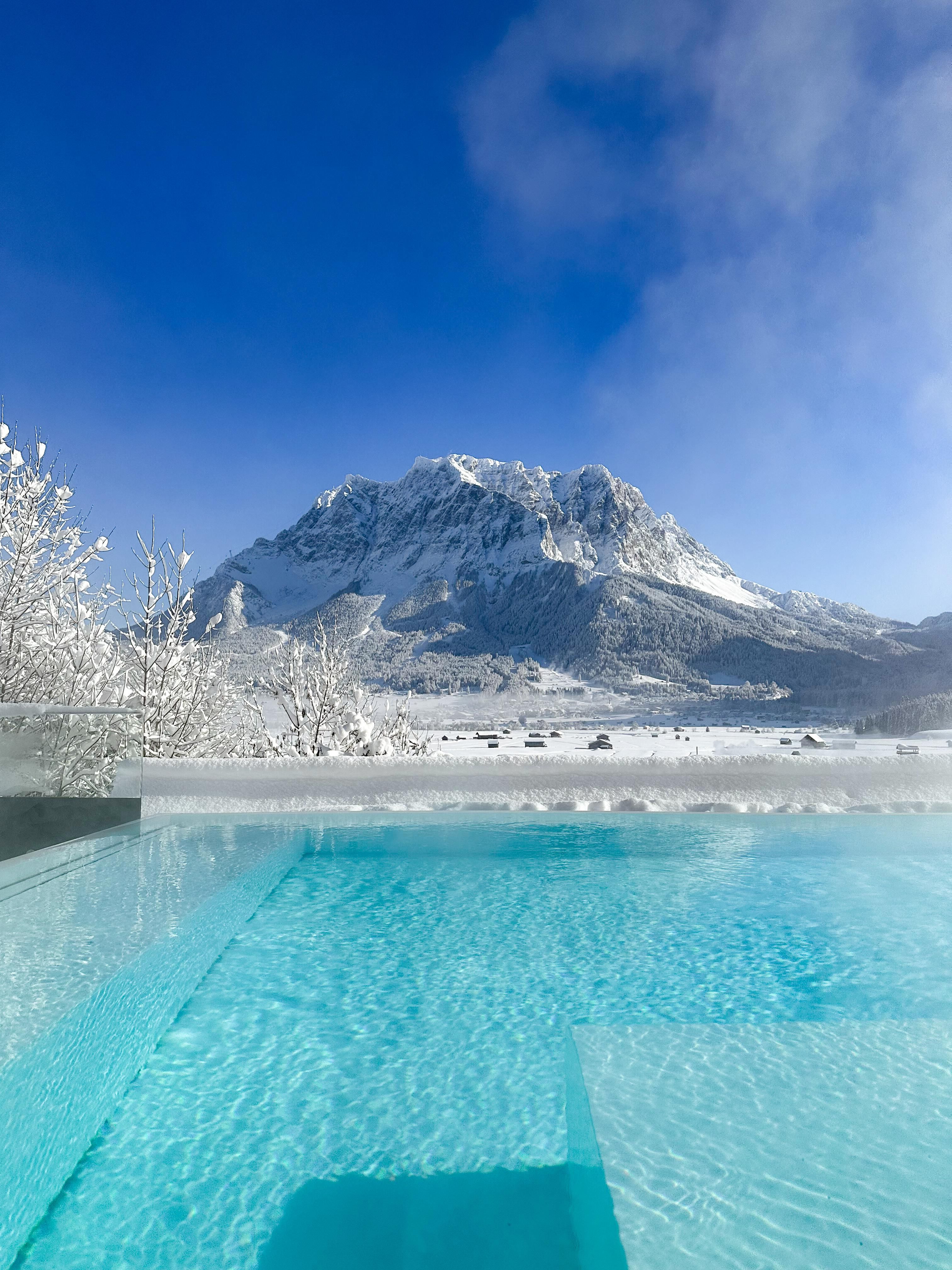 A clear pool in front of a snow-covered landscape and a high mountain. The radiant blue sky complements the wintry scenery.