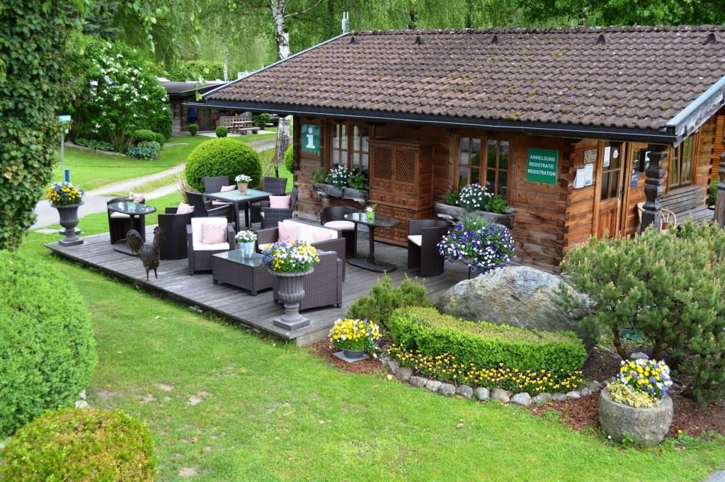 A cozy wooden house with a terrace equipped with comfortable furniture. Lawn and colorful flowers surround the area, creating an inviting atmosphere.