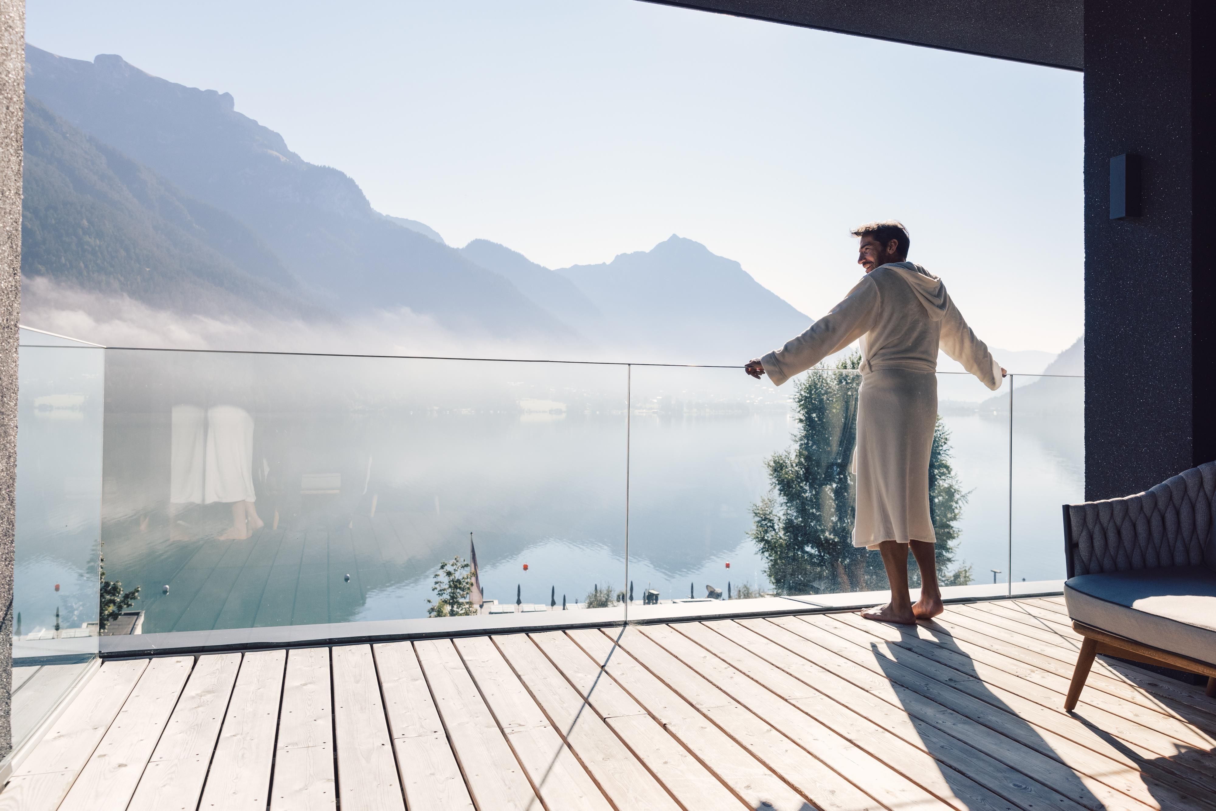 A person is standing on a balcony and looking at a foggy lake and mountains. It is a quiet and relaxing moment in nature.