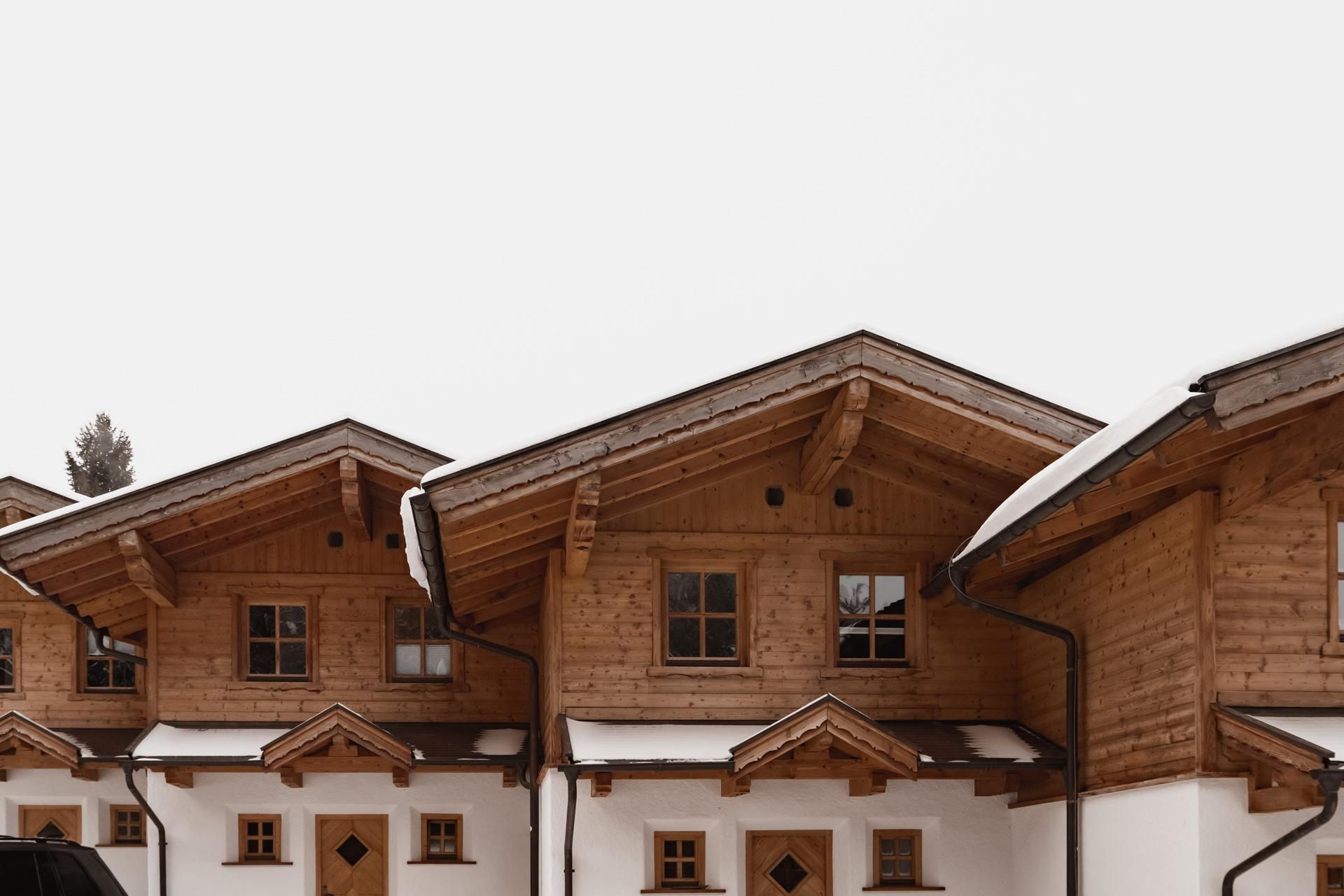A row of wooden chalets with snow-covered roofs. The facades are traditionally designed and exude coziness.