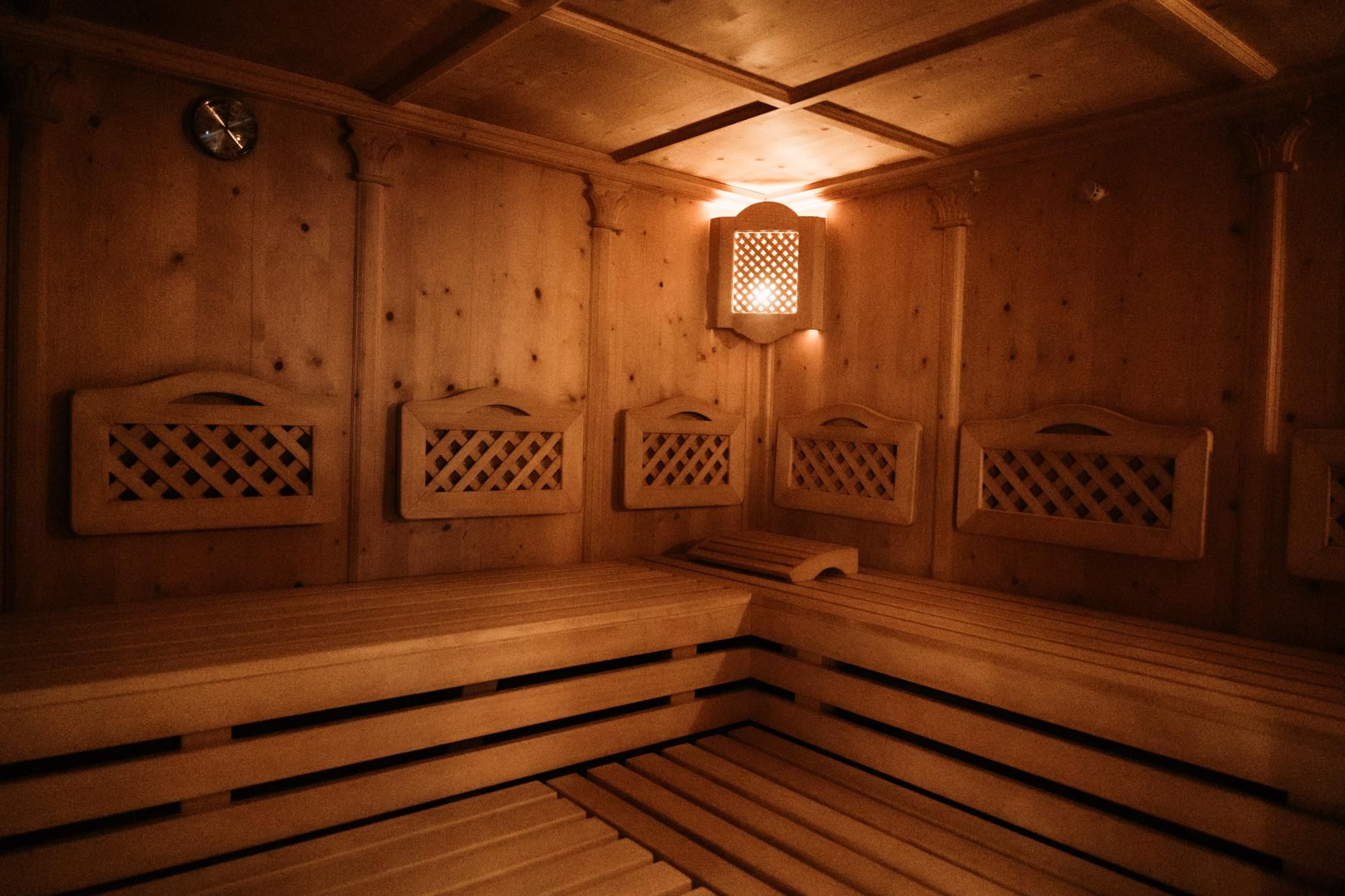 A cozy sauna with a wooden bench and soft lighting. The walls are made of light wood, creating a relaxing atmosphere.