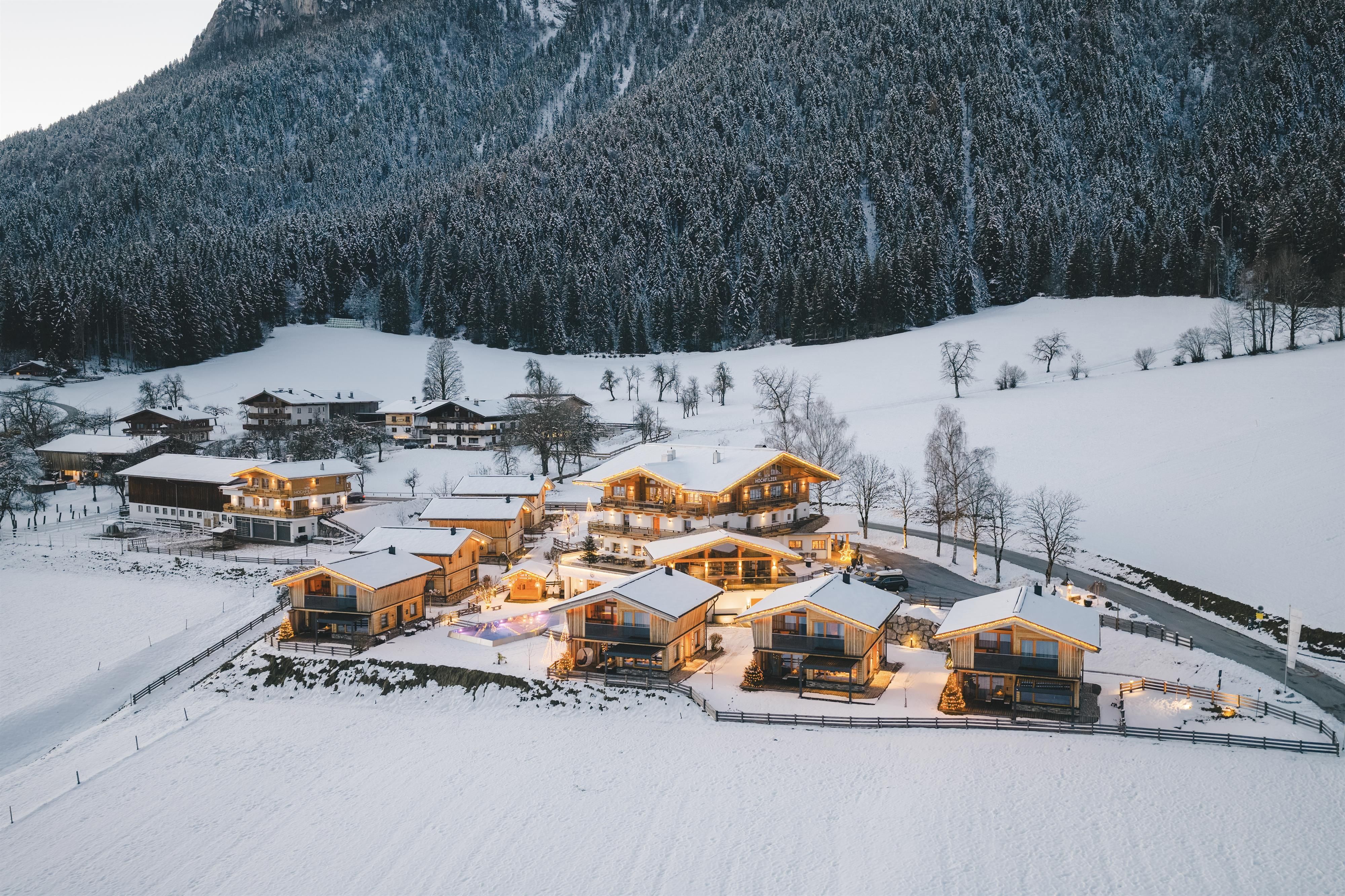 A picturesque winter landscape with snow-covered cottages. The little houses are cozily lit and surrounded by mountains.