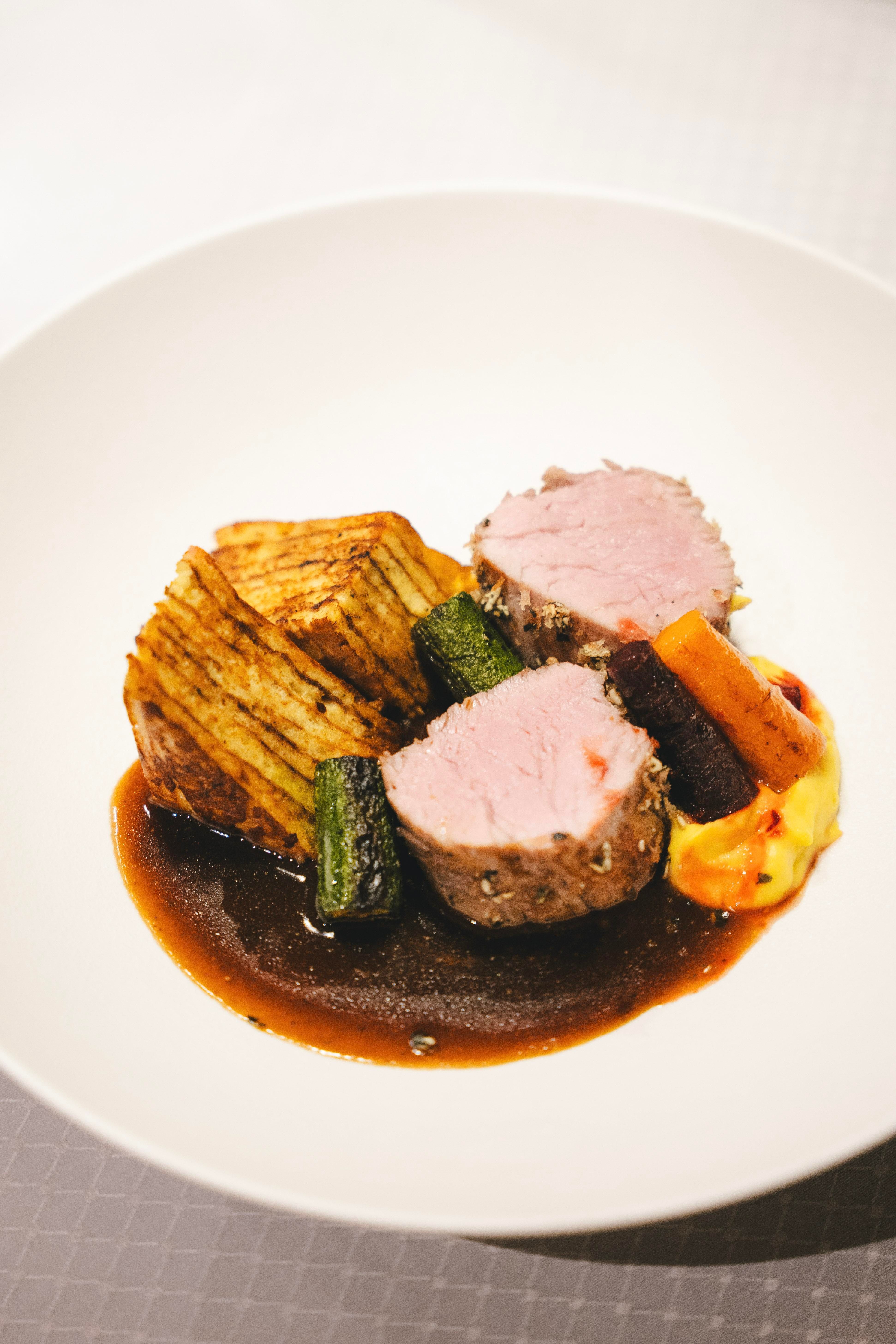 A creatively arranged dish with tender meat, sautéed vegetables, and a dark sauce. Served with potatoes in the form of slices.